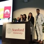 Five people stand behind a podium that says "Stanford University."