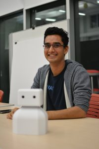 Akhil sitting at a table and smiling; on the table is a robot model.
