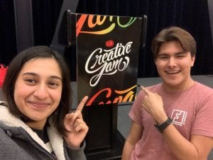Two young adults point at a sign that says "Creative Jam"