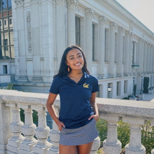 Young girl wearing a navy blue Cal polo shirt stands in front of Doe library building on UC Berkeley campus